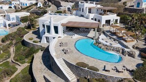 Luftaufnahme eines Resorts mit großem Schwimmbecken, weißen Gebäuden und einem Kiesweg.