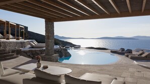 Ein Poolbereich mit einer Steinstruktur, Liegestühlen und Blick auf das Meer.