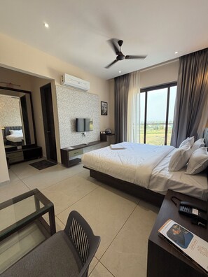 A modern hotel room with a bed, a desk, a chair, a TV, and a ceiling fan.