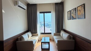 Una sala de estar moderna con ventilador de techo, dos sofás, una mesa de centro y un amplio ventanal con cortinas.