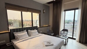 Una habitación de hotel moderna con una cama grande, un ventilador de techo, vistas de la ciudad y una zona de estar con una silla.