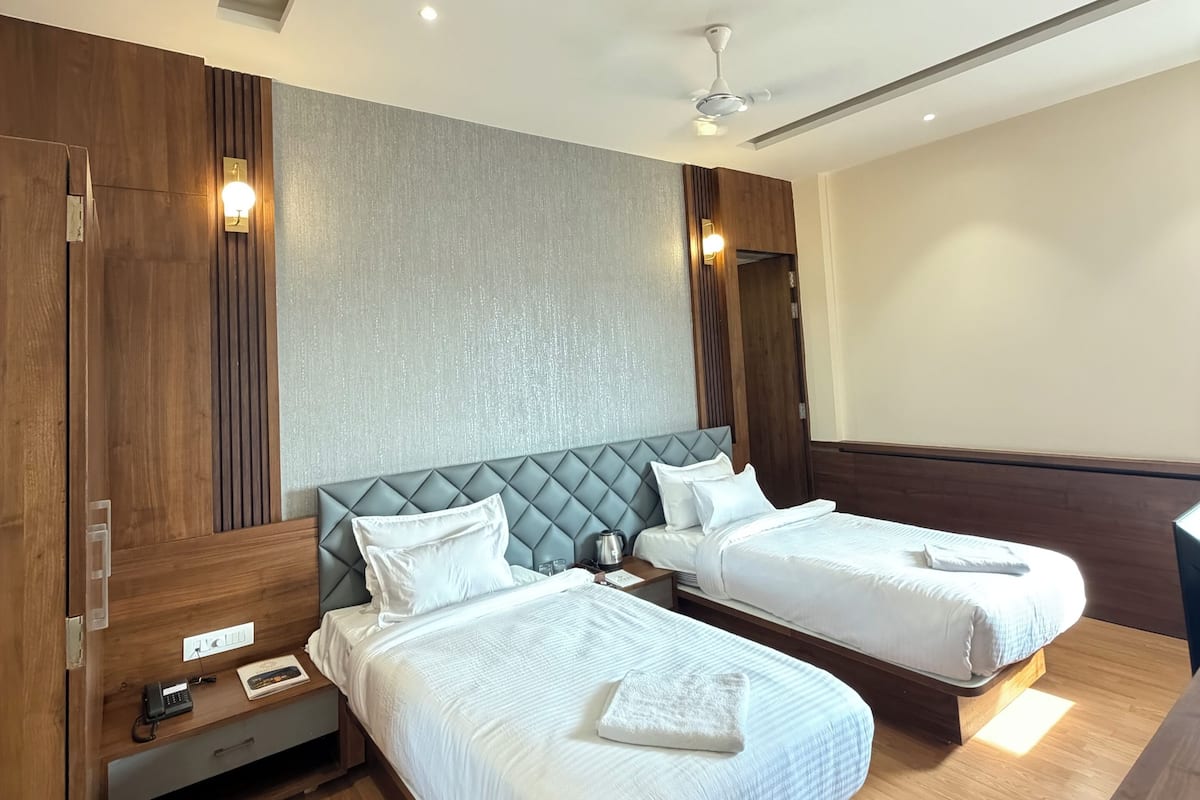 Habitación de hotel con dos camas, piso de madera, ventilador de techo y una lámpara fijada a la pared.