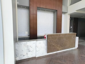 A reception desk with a marble and wood finish, a red object on the counter, and a patterned wall behind.