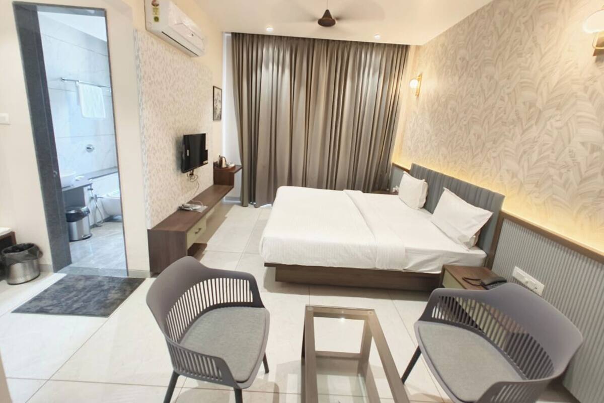 Una habitación de hotel moderna con una cama grande, dos sillones, una mesita y un televisor.