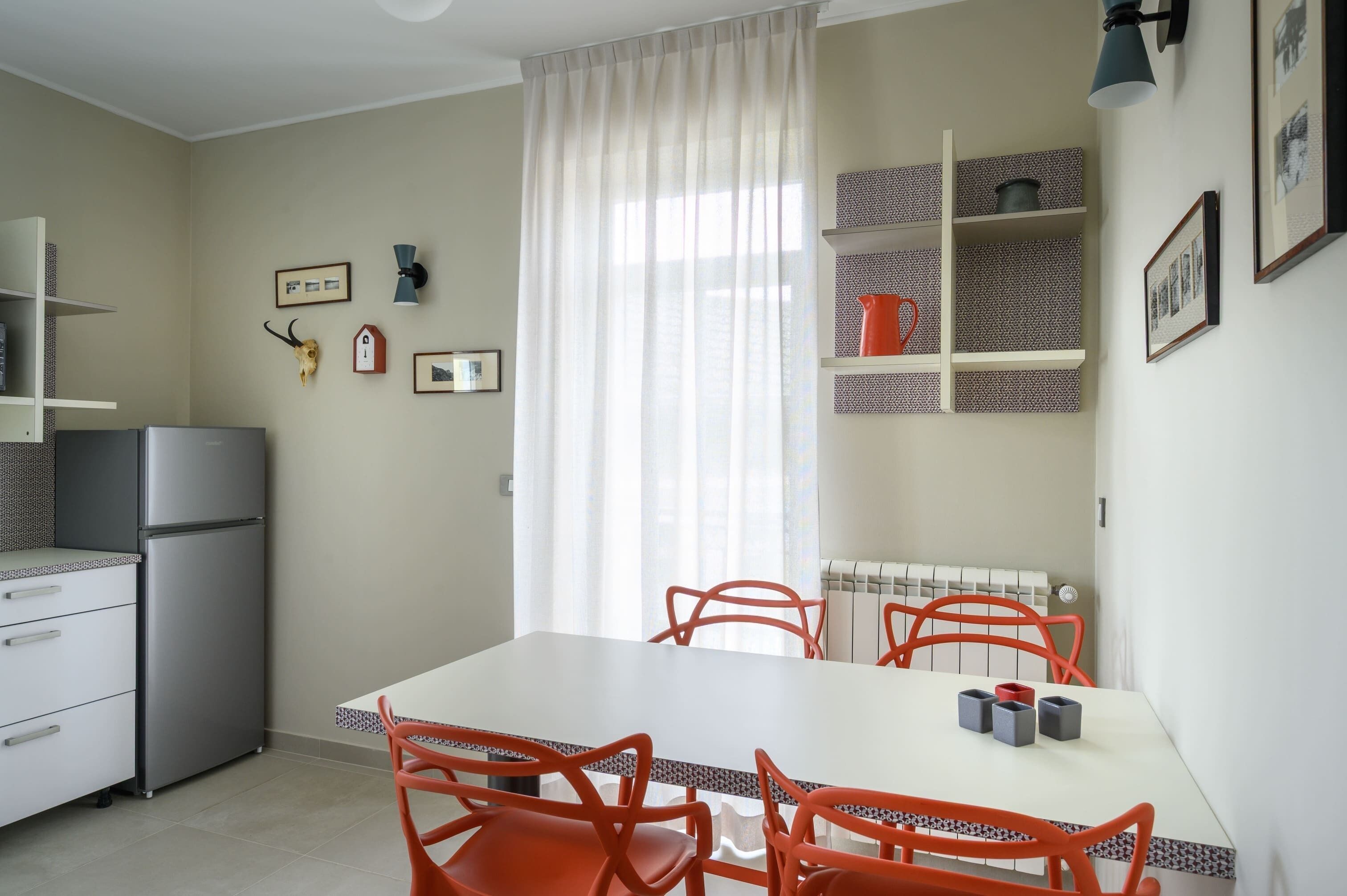 A compact kitchen with a refrigerator, a dining table with chairs, and a radiator.