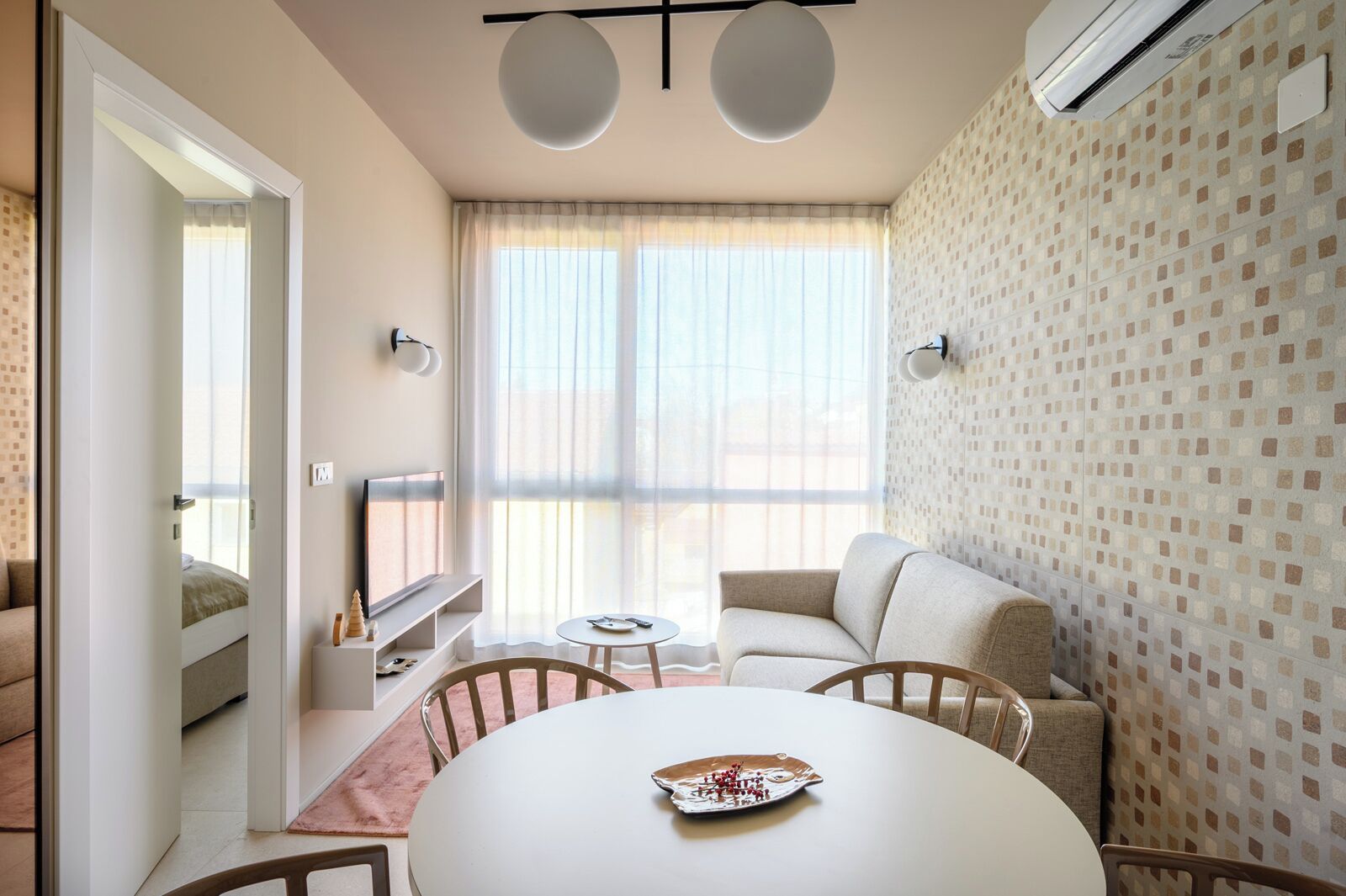 A modern living room with a sofa, a TV, a dining table with a plate, and a patterned wall.