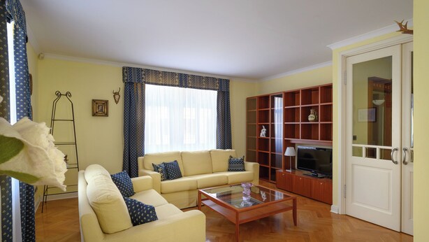 Uma sala de estar com um sofá, uma mesa de centro de vidro, uma televisão e uma estante de livros.