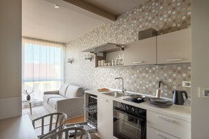 Una cocina moderna con horno empotrado, zona de comedor con sofá y ventana con cortinas de gasa.