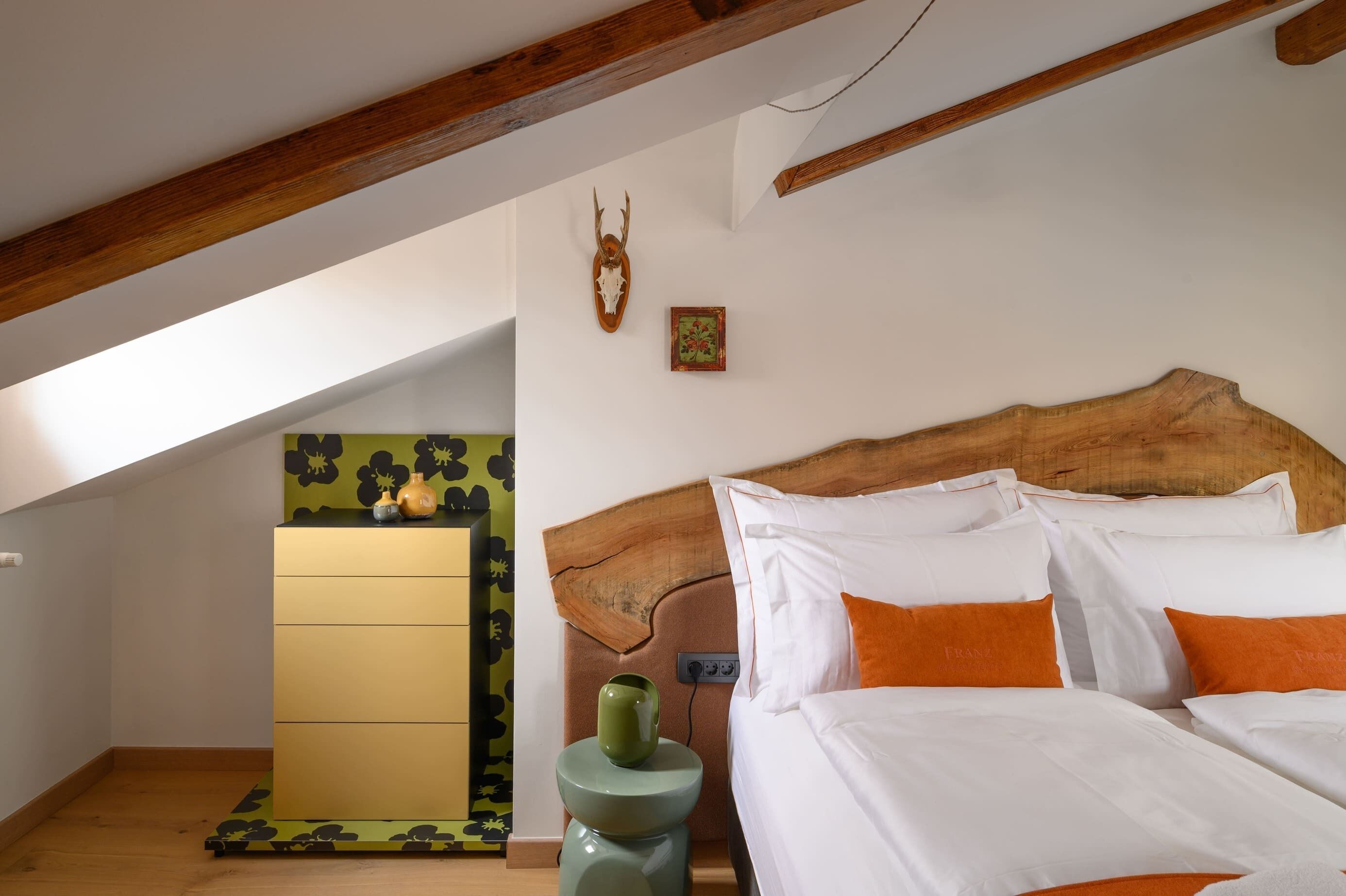 A bedroom with a wooden headboard, white bedding, and an orange pillow.