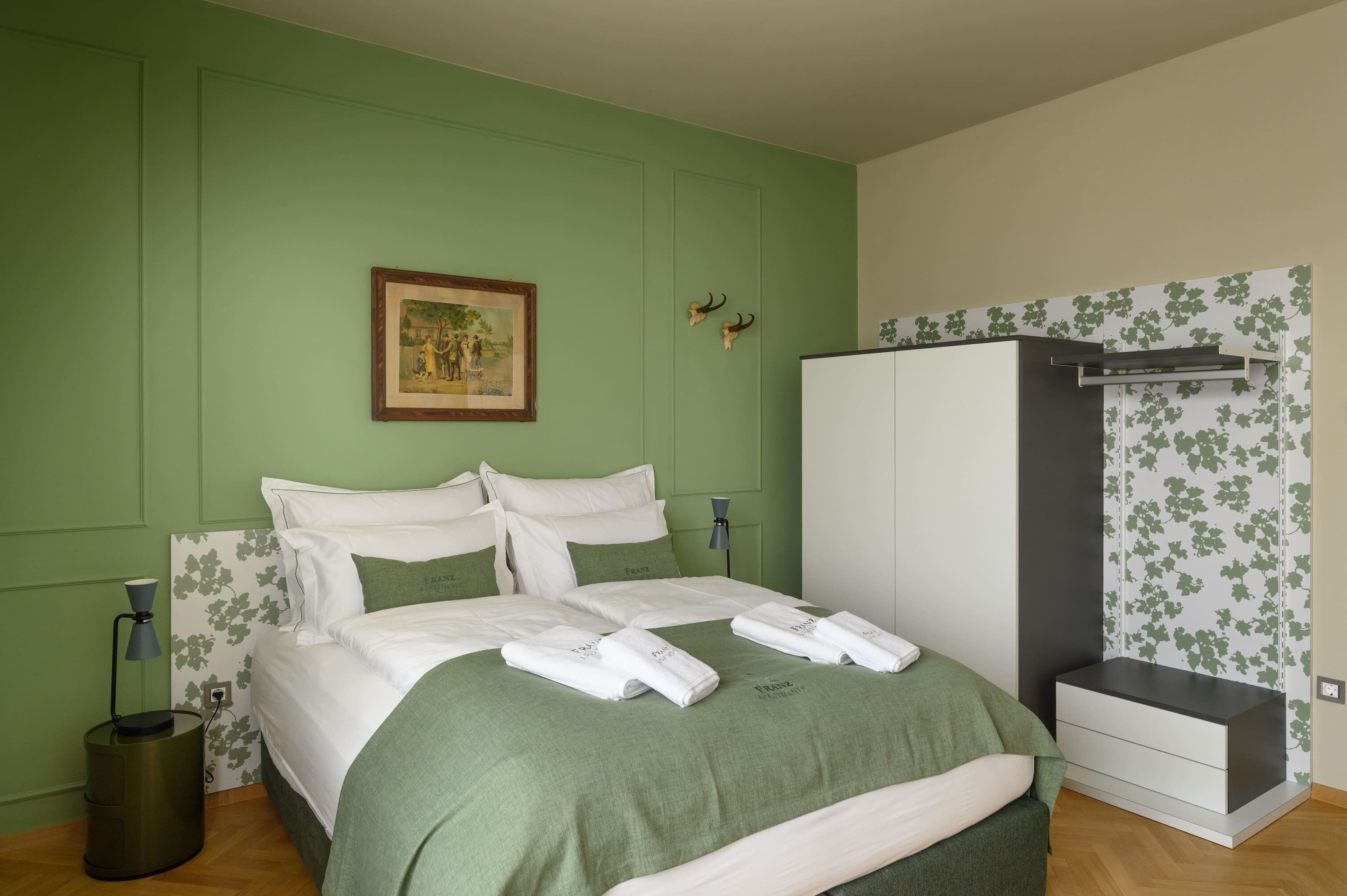 Ein ordentlich eingerichtetes Schlafzimmer mit Bett, Schrank, Nachttisch und einem gerahmten Bild an der Wand.