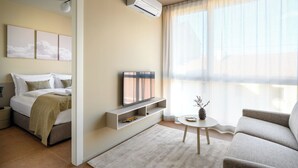 A modern hotel room with a bed, a TV, a small table with a vase, and a large window with sheer curtains. - Franz Apartments  (Ilirska Bistrica)
