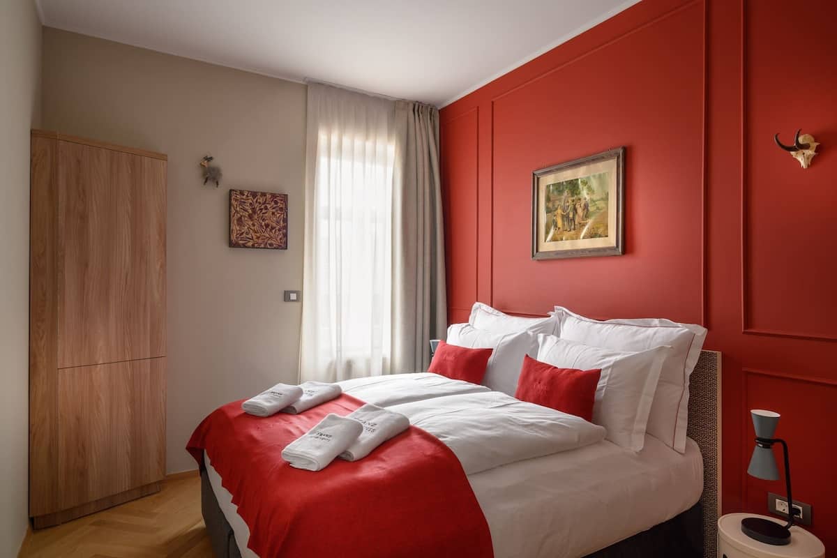 Un dormitorio con cama, ropa de cama roja y blanca, un armario de madera, un cuadro y una decoración de calavera en la pared.