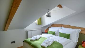 Un dormitorio con techo inclinado, cama con ropa de cama verde y blanca, una mesita con un objeto rojo y una lámpara colgante.
