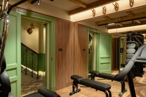 Ein Fitnessraum mit Trainingsgeräten, einer Holzwand und einer Treppe mit grünen Türen.