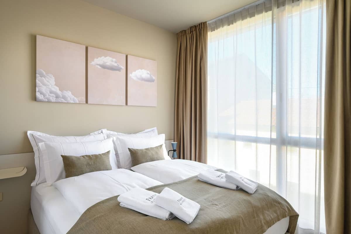 Habitación de hotel con una cama grande, cortinas color beige y vistas al exterior.