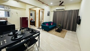 Ein modernes Wohnzimmer mit Essbereich, einem türkisfarbenen Sofa und einem Deckenventilator.