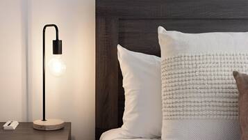 A neatly made bed with white and beige pillows, a dark wooden headboard, and a modern floor lamp with a light bulb on a bedside table.