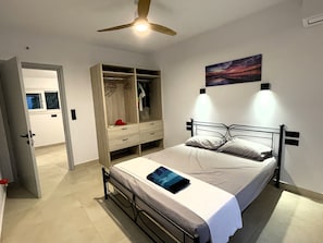 A bedroom with a bed, a wardrobe, a ceiling fan, and a painting on the wall.