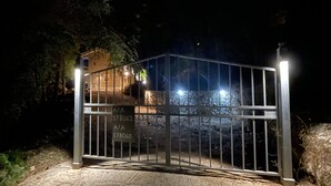 En metalport med et skilt, en belagt sti og en bygning i baggrunden.
