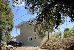 A house with a stone wall, a parked car, and trees.