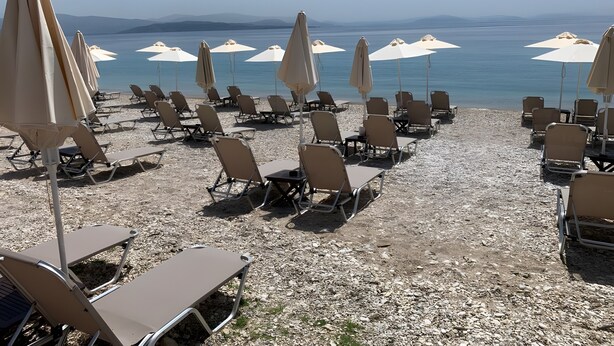A beach with rows of sun loungers and umbrellas, a clear view of the sea, and a rocky shoreline. - Holiday Home 'Modern Single-story Villa' with Wi-Fi (Mparmpati)