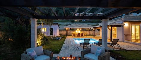 Une terrasse extérieure couverte, aménagée avec des meubles en osier, une piscine et un chemin en pierre.