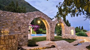 Estructura de piedra con arcos, piscina y montañas al fondo.