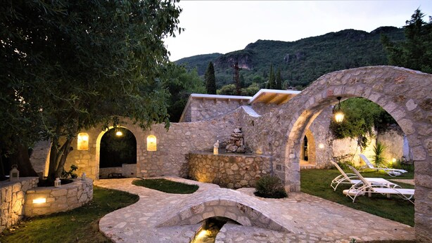 Un puente de piedra, arcos y una zona de piscina con sillones de relax.