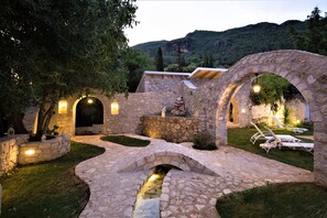 Un puente de piedra, arcos y una zona de piscina con sillones de relax.