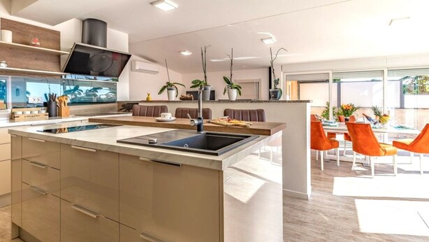 Una cocina moderna con una isla central, electrodomésticos integrados y un comedor con sillas naranjas.