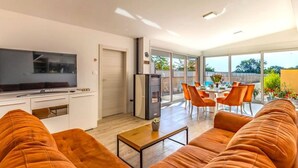 Una sala de estar moderna con sofá, televisor de pantalla plana, una zona de cocina y un comedor con sillas.