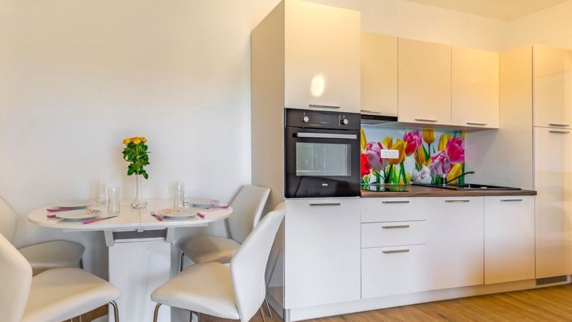 Uma cozinha moderna com armários brancos, forno embutido e painel de cozinha colorido.
