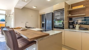 A modern kitchen with a central island, built-in appliances, and a dining area with chairs. - Villa Matošic by Villas Guide (Medulin)