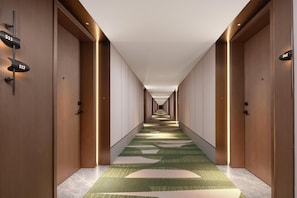 Pasillo de hotel con puertas de madera, placas de números de habitaciones y una alfombra estampada.
