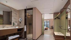 Un baño de hotel moderno con un espejo grande, un tocador redondo, ducha y vista a la ciudad.