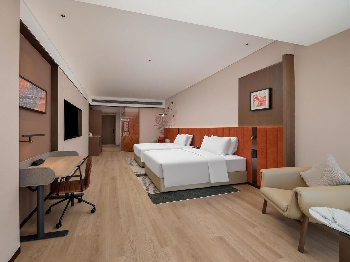 Et moderne hotelværelse med et skrivebord, to senge, en stol og kunst på væggene.