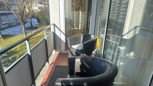 A balcony with two black chairs, a small table, and a glass door leading to a room. - Room-in the Heart of the City of Salzbur (Salzburg)