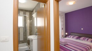 Ein Schlafzimmer mit Bett, ein Badezimmer mit Dusche und einer violetten Wand.