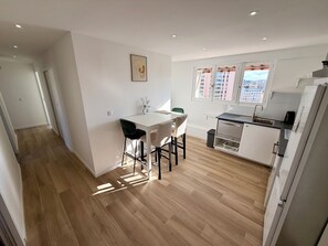 A modern kitchen with a dining area, wooden flooring, and a view of buildings through the window. - Upscale 4-bedroom apartment with large balcony (Toulon)