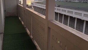 Un balcó amb gespa artificial verda, baranes blanques i una vista d'un passeig marítim amb edificis i un capvespre.