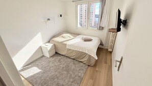 Un dormitori amb llit, una taula de nit, un radiador i una finestra amb cortines.