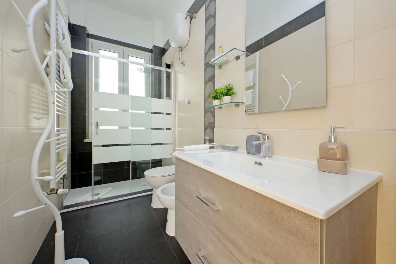Un baño moderno con cabina de ducha de vidrio, lavabo blanco y tocador color beige.