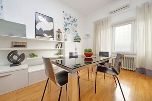 Un comedor moderno con una mesa de vidrio, sillas negras, armarios blancos y obras de arte en las paredes.