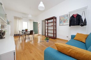 A modern living room with a blue sofa, wooden floor, and a dining area with a table and chairs. - Nice flat with Patio near Vatican (roma)