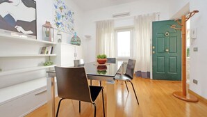 Ein modernes Wohnzimmer mit einem Glastisch, zwei Stühlen, einer grünen Tür und einer weißen Wand mit Kunstwerken.