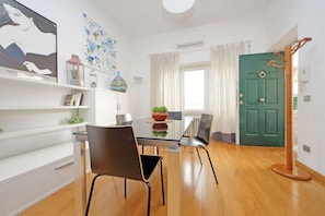 Ein modernes Wohnzimmer mit einem Glastisch, zwei Stühlen, einer grünen Tür und einer weißen Wand mit Kunstwerken.