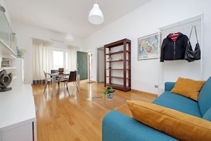 Ein modernes Wohnzimmer mit einem blauen Sofa, Holzboden und einem Essbereich mit Tisch und Stühlen.