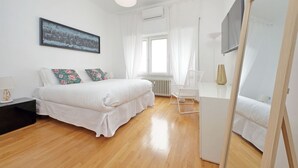 Ein Schlafzimmer mit Bett, Nachttisch, Sessel, Fenster mit Vorhängen, Heizkörper und Spiegel.