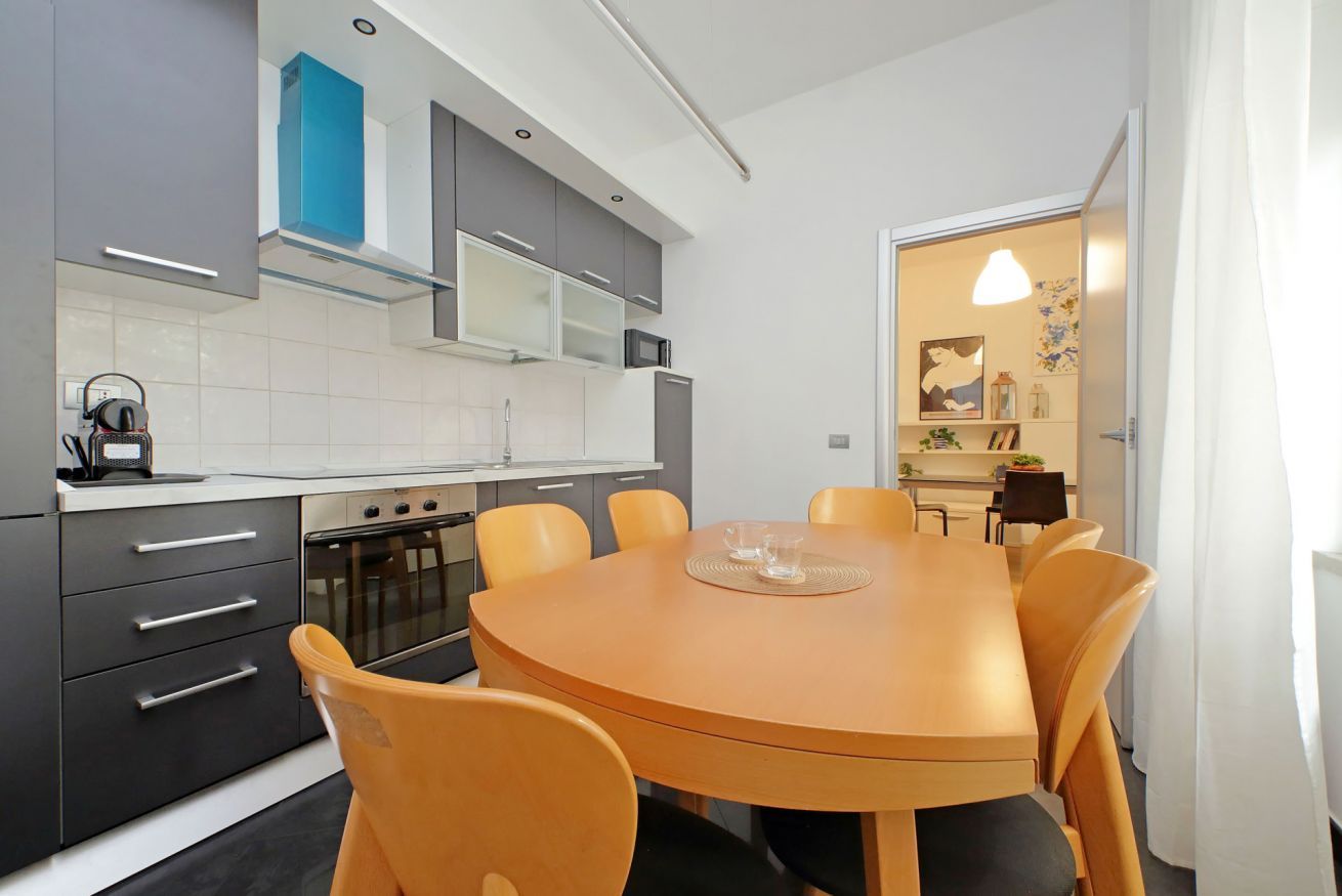 Una cocina moderna con armarios grises, una mesa redonda de madera y sillas naranjas.
