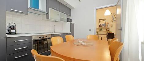 Una cocina moderna con armarios grises, una mesa redonda de madera y sillas naranjas.